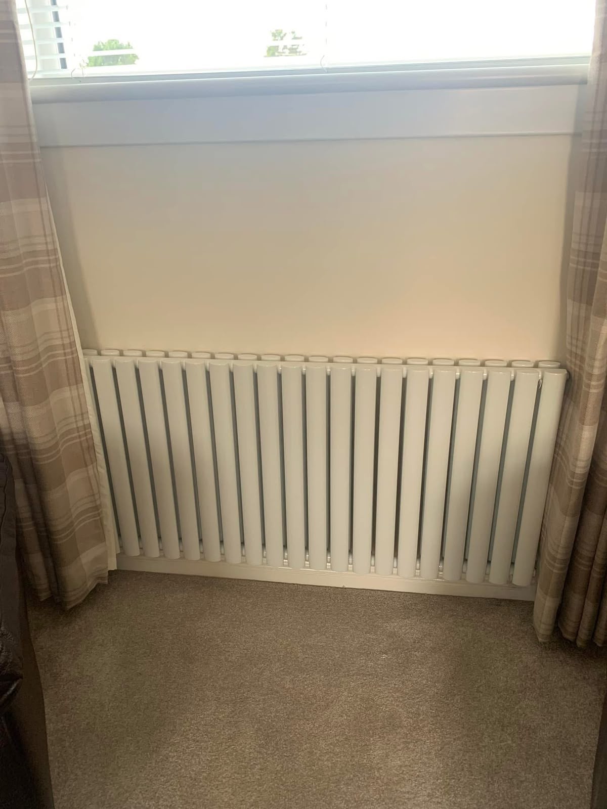 White column radiator fitted beneath a window in a carpeted living room