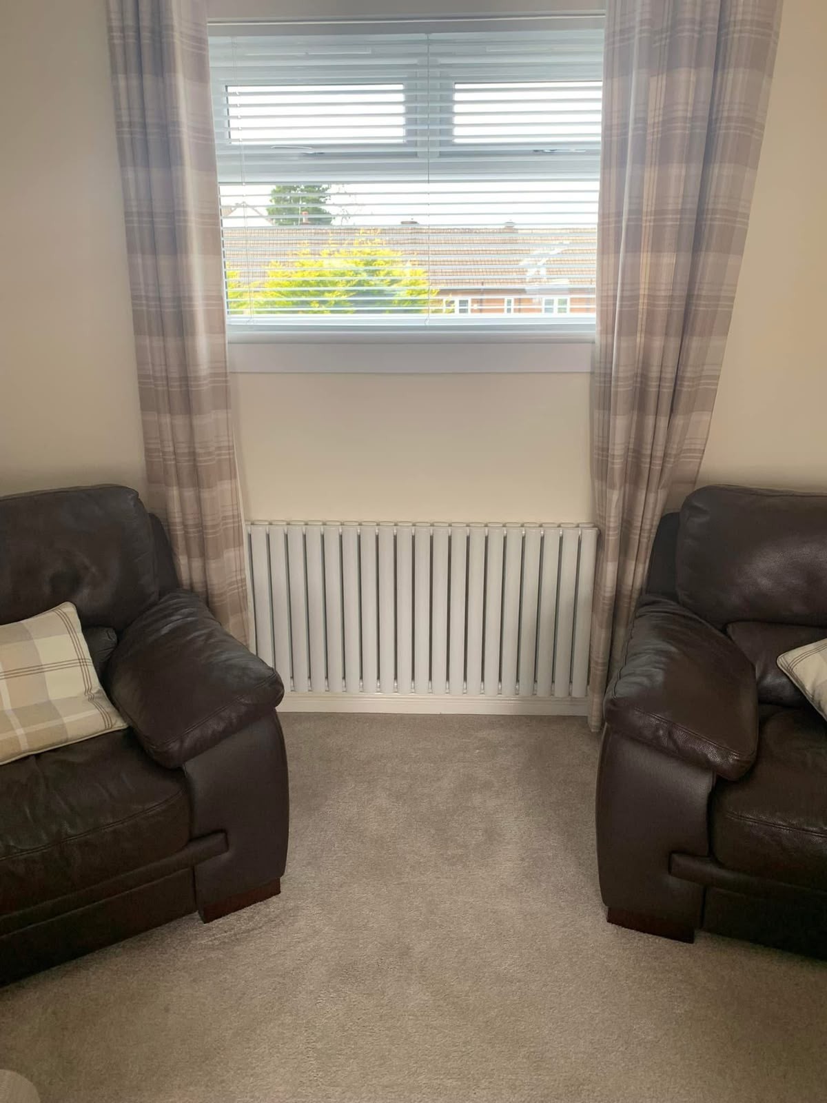 White panel radiator fitted under a living room window between leather sofas