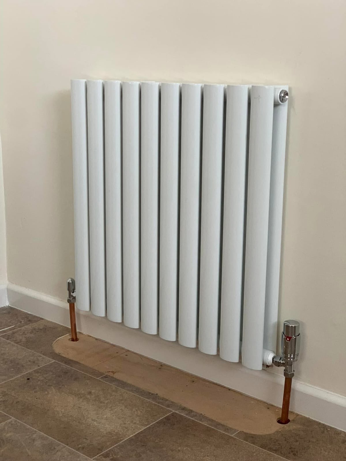 White oval column designer radiator installed with copper pipework on a tiled floor