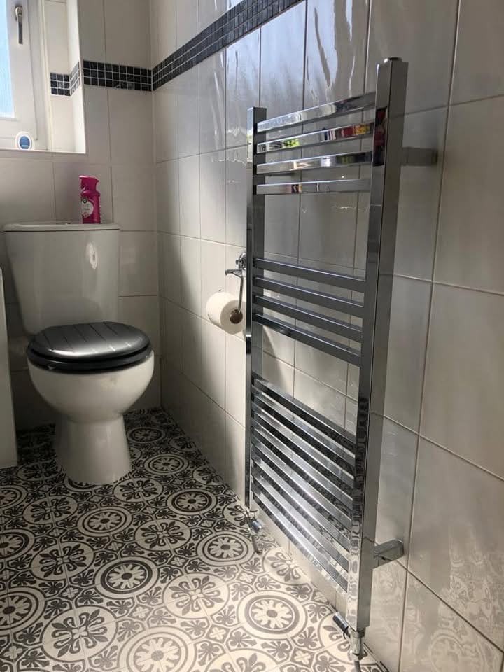 Chrome heated towel rail installed in a bathroom with patterned floor tiles