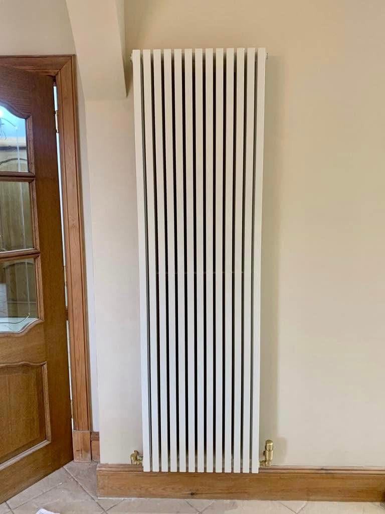 Tall vertical white designer radiator installed beside an internal door
